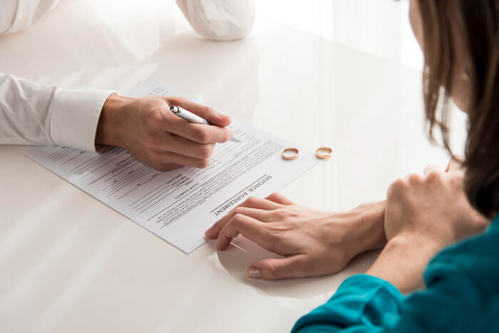Two people discussing an under agreement document with wedding rings on the table, symbolizing betrayal and shock.