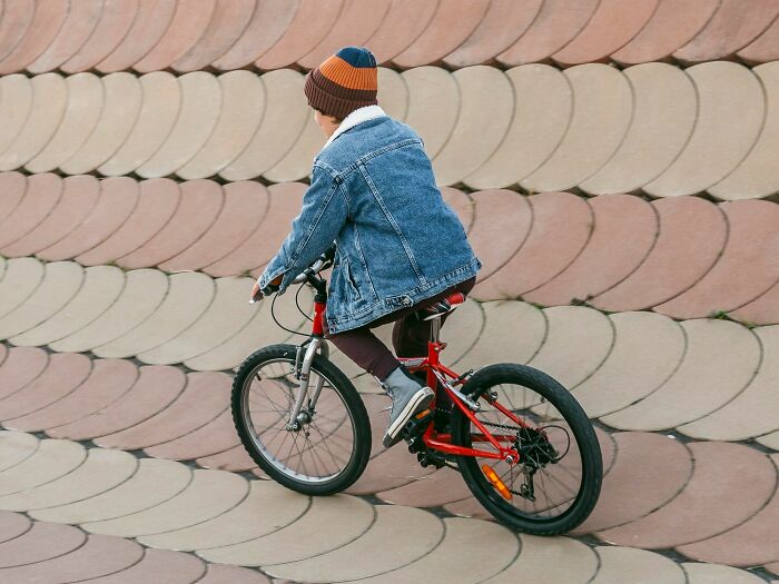 A young person in a denim jacket and striped hat rides a red bicycle, illustrating rumours heard and wild experiences.