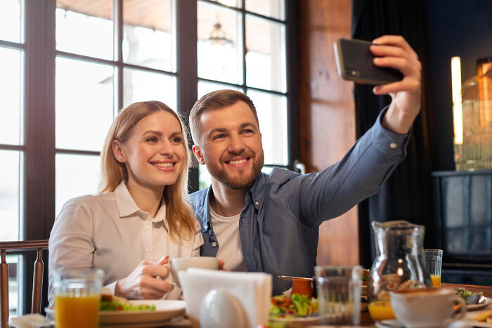 Couple smiling and taking a selfie during a first date in a cozy cafe, highlighting common first date red flags.
