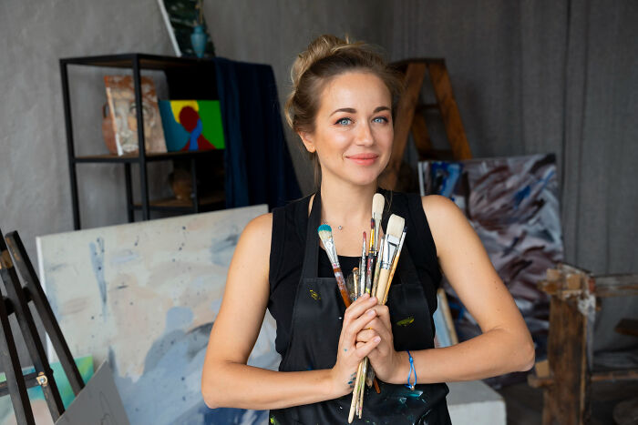 Young woman thriving as an artist, holding paintbrushes in a creative studio, embodying inspiring comebacks and success.