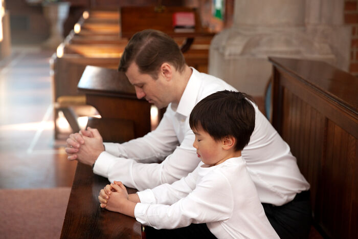 A man and a young boy kneeling in church, hands clasped in prayer. Many former priests and nuns leave the Church.