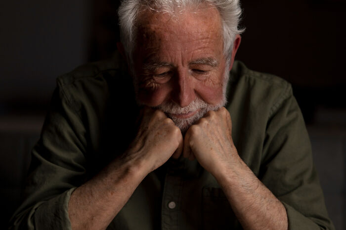 Elderly man with gray hair looking down sadly, reflecting on moments of good person betrayal and emotional shock.