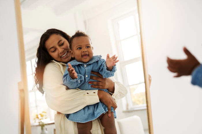 Mother holding baby girl smiling in front of mirror, capturing a joyful moment on a memorable first date experience.