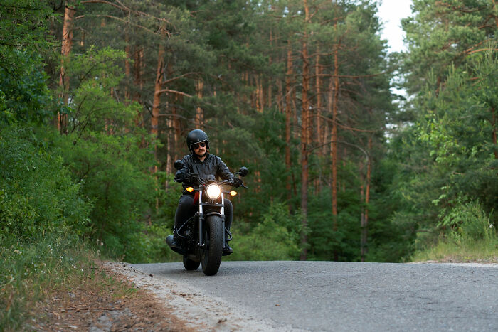 A motorcyclist in a helmet and sunglasses riding on a winding road through a forest. Avoid disturbing sounds.