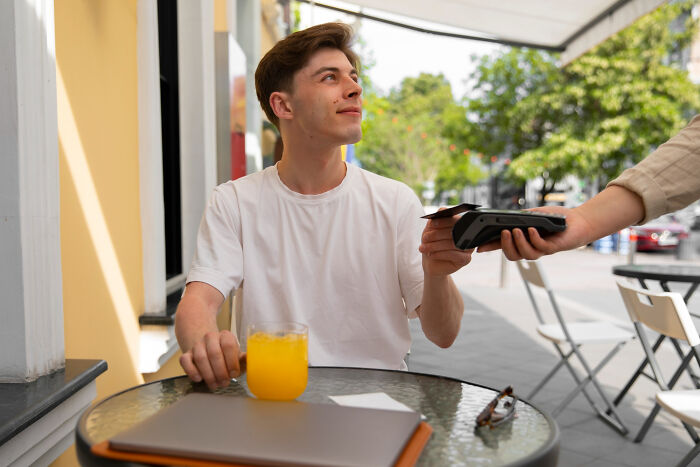 Young man on a first date reluctantly paying with card outdoors, depicting red flags and instant regret moments