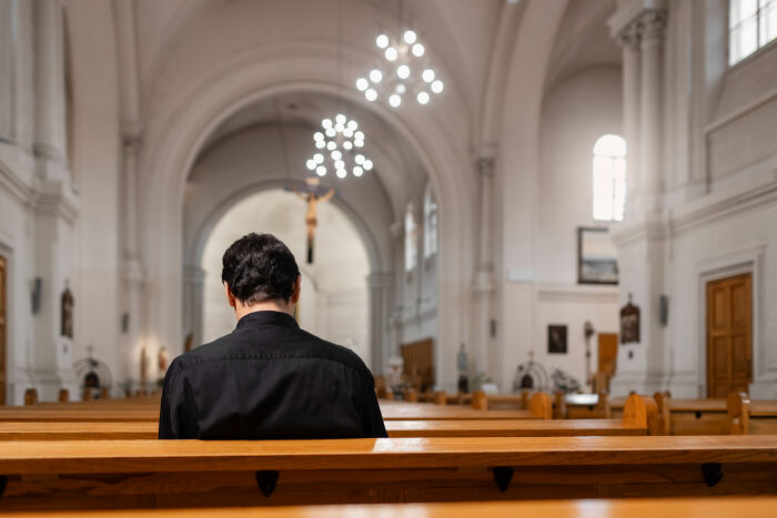 A man in a black shirt sits in a church pew, his back to the viewer, reflecting on why priests leave the church.