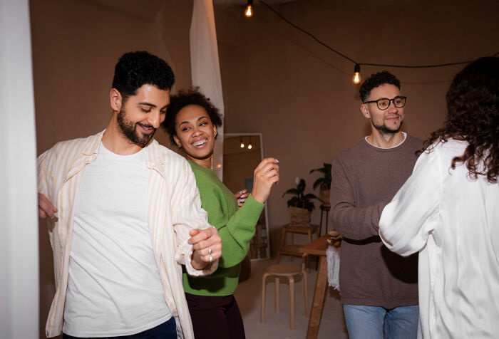 Group of young adults on a first date gathering, smiling and dancing in a cozy indoor setting with warm lighting.