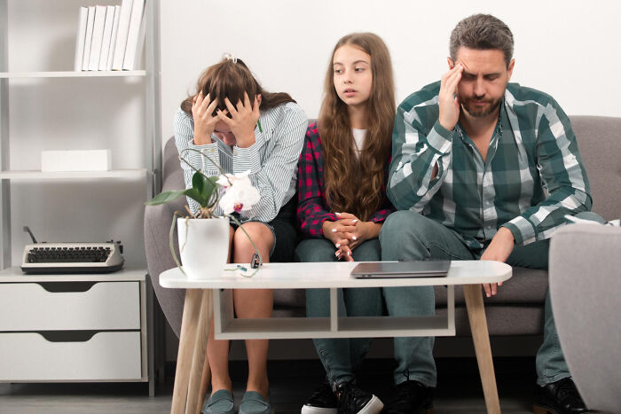 Family with celebrity relatives looking distressed on a couch. A woman covers her face, a girl watches, and a man holds his head.