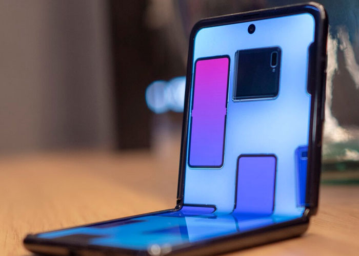 Foldable smartphone placed on a wooden surface with reflections indicating signs related to the economy not doing well.