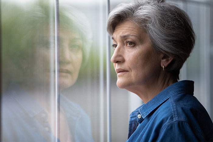 Middle-aged woman reflecting by window, sharing a dramatic story about her mom, evoking soap opera emotions.