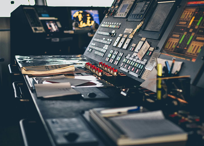 A control room with multiple screens and a large console with numerous buttons and levers, showing exclusive access.