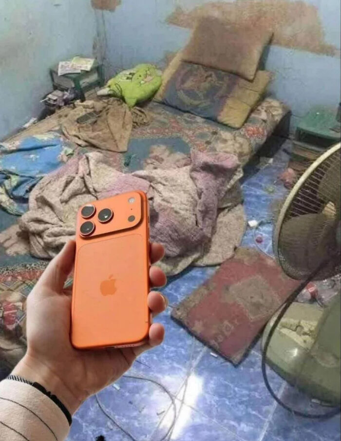 A hand holds an orange iPhone in a messy room, making people go "hmmm". It's one of those weird images.