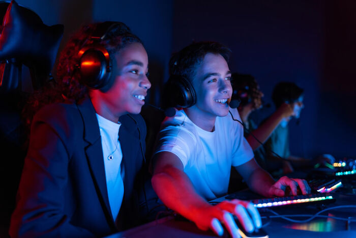 Two young gamers wearing headsets play together in a dimly lit room, showing random life decisions leading to success.