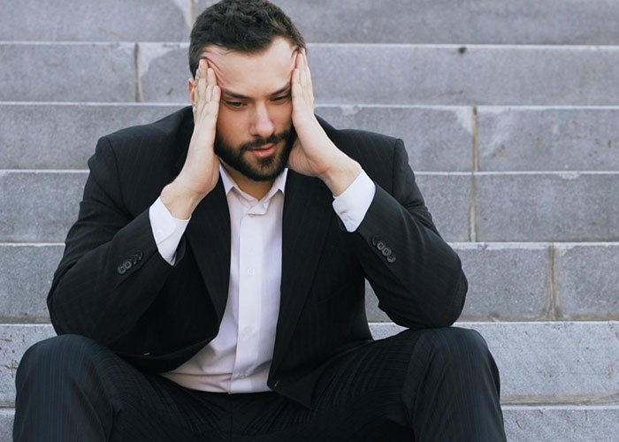 Man in a suit sitting on steps holding his head, reflecting concern about signs of the struggling economy.