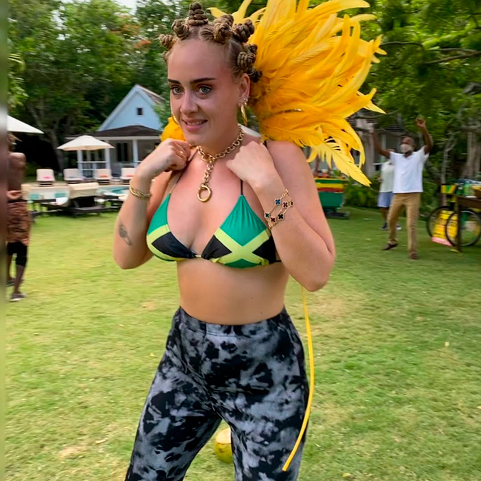 Adele in a Jamaican flag bikini top and tie-dye leggings, with yellow feathers and Bantu knots, looking happy, 6 years ago.