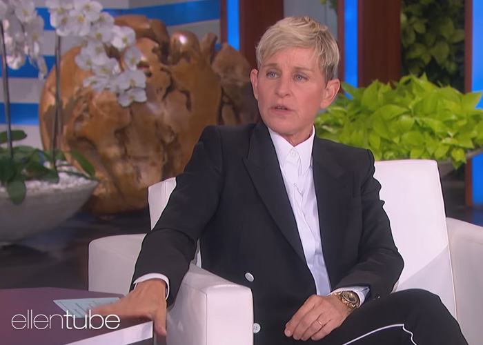 Ellen DeGeneres looking thoughtful on her show, discussing things that went down 6 years ago, wearing a black suit.