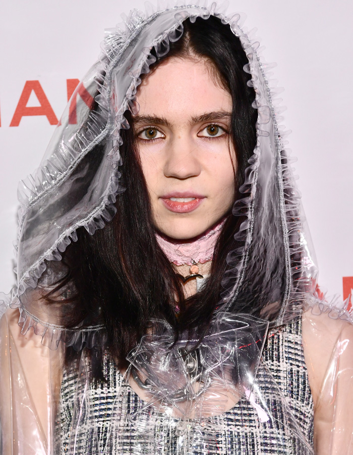 A woman with dark hair in a clear plastic ruffled hood and coat. Her look is unreal today, 6 years ago.