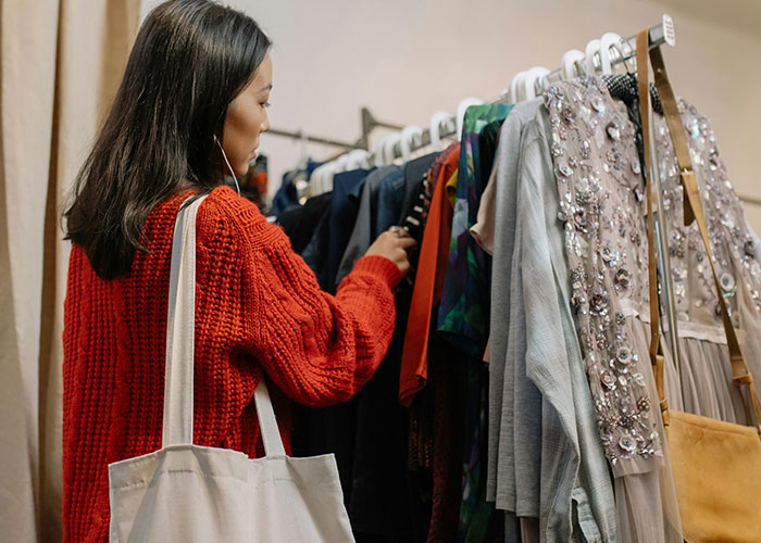 Woman in a red sweater browsing clothing rack, illustrating signs that show the economy may not be doing well.