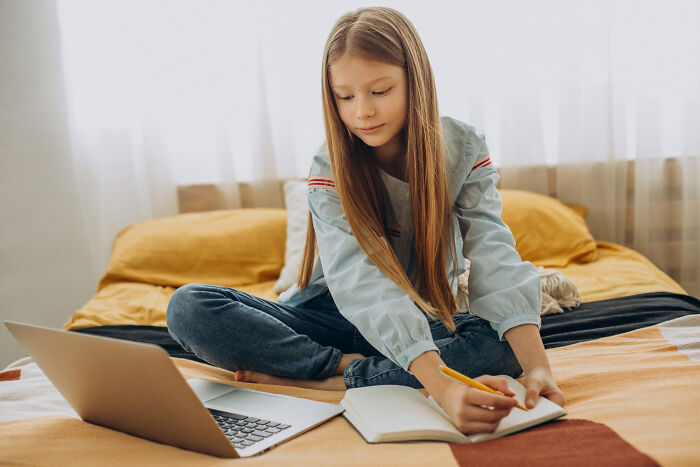 Young girl sitting on bed with laptop and notebook, illustrating inspiring comebacks and thriving success concept.