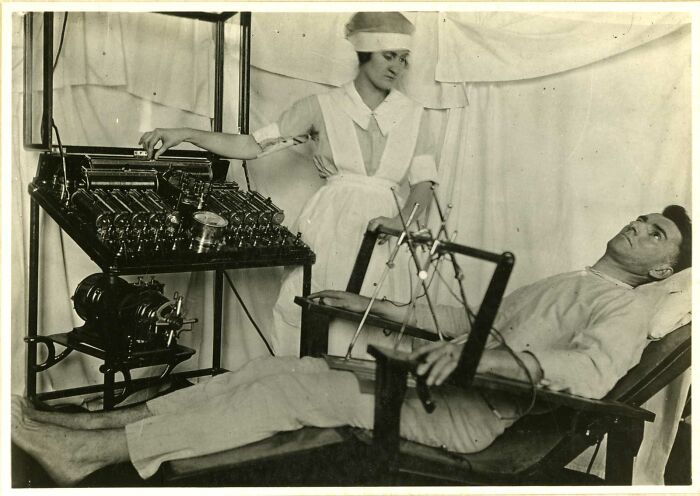 Vintage medical device in use with nurse operating early healthcare equipment on a reclining patient in black and white.