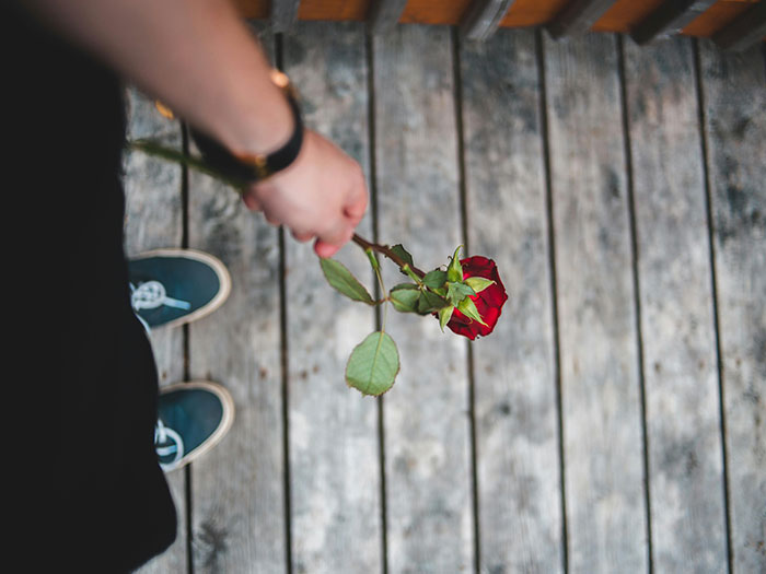 A person holding a wilting red rose, standing on wooden planks. Symbolizes horrible first dates.
