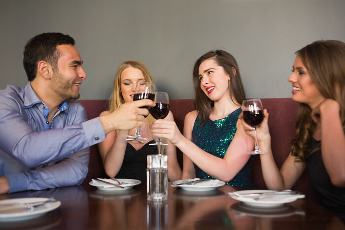 Four friends clinking wine glasses at a restaurant table, capturing the theme of first dates with red flags and regret.
