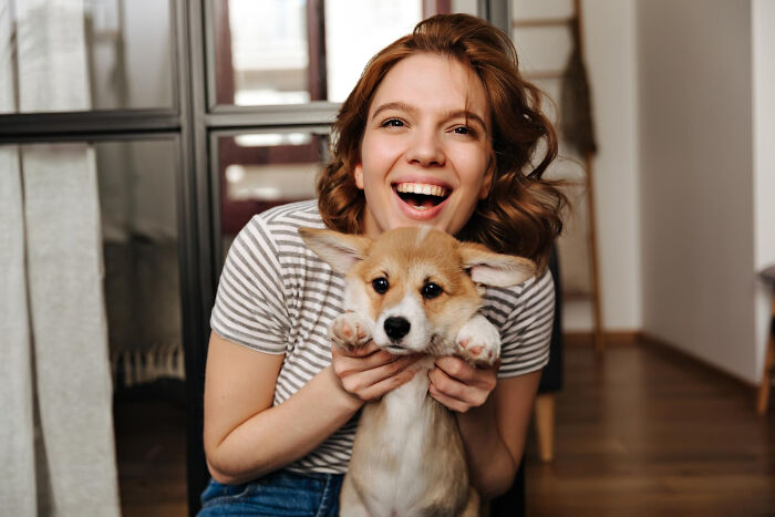 Happy young woman holding a cute puppy indoors, symbolizing inspiring comebacks and thriving moments.