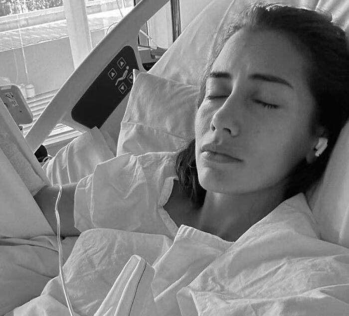 Young woman resting in hospital bed with eyes closed, sharing urgent warning about going to nail salons after incident.