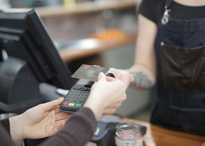 Customer using credit card with a card reader at a cafe counter representing signs of the economy not doing well.
