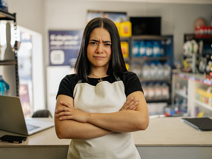 Woman staff member with arms crossed, showing silent satisfaction after dealing with rude customers in a store setting.