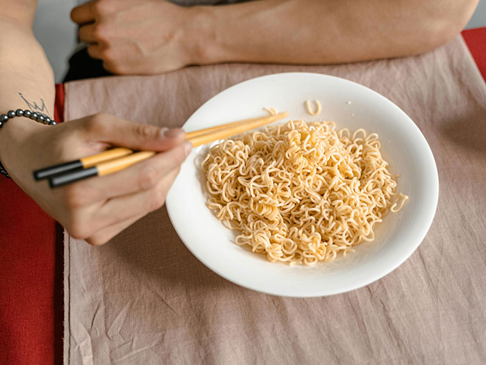 A person eating ramen noodles with chopsticks, symbolizing a potentially horrible first date scenario.