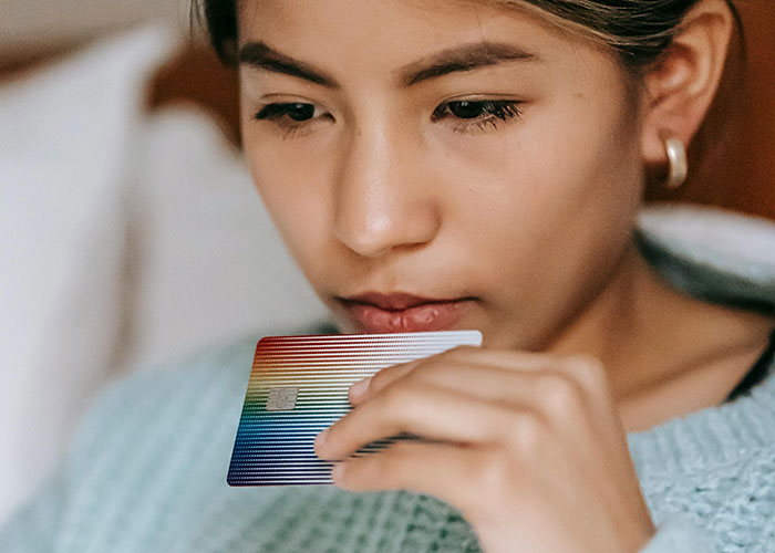 Young woman holding a colorful credit card, contemplating a wedding dress purchase and tipping decision at home.