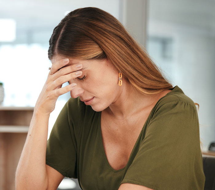 Uma mulher parece angustiada, com a mão na testa, pensando no filho secreto do marido.