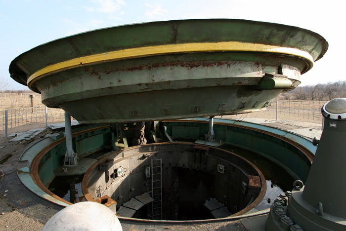 Abandoned military missile silo representing massive betrayals in human history with rusted metal and empty surroundings.