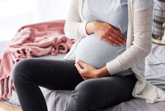 Pregnant woman sitting on bed with hands on belly, illustrating challenges women face in communication with men.