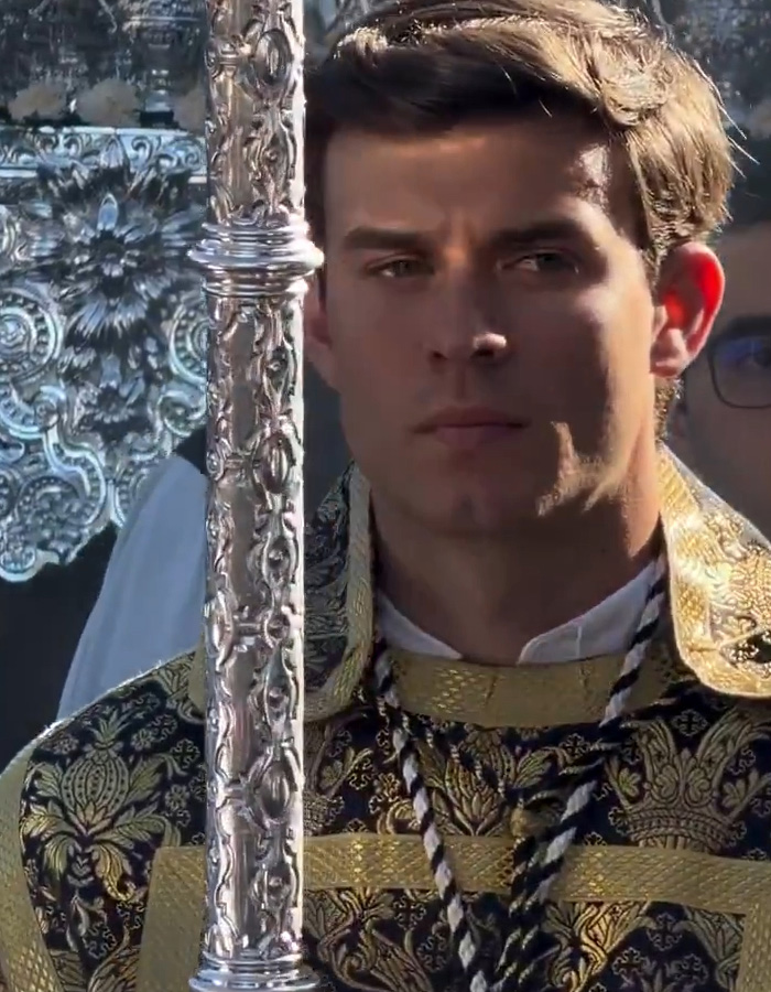 Jovem vestido com vestimentas ornamentadas segurando um cajado de prata durante uma procissão de Páscoa na Espanha, atraindo a atenção da Internet.