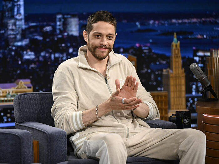 Pete Davidson speaking on a talk show set, sparking debate about watching adult content with a daughter.