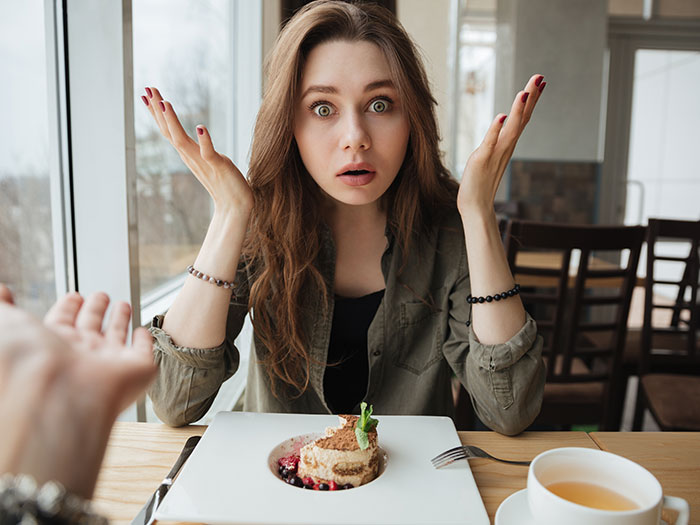 A woman with wide eyes and open palms, reacting to a horrible first date, with dessert on the table.