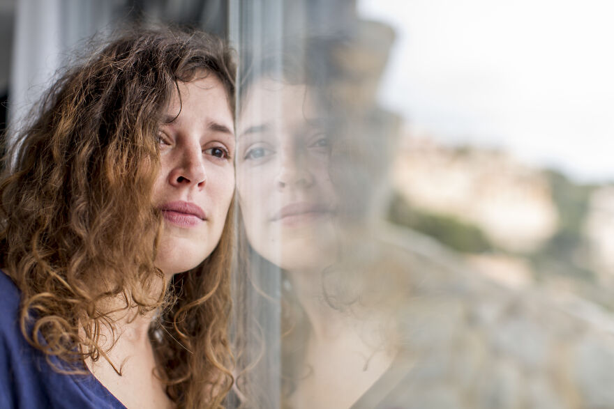 Woman with curly hair looking out window thoughtfully, reflecting on feeling like the outcast and ways to thrive independently.