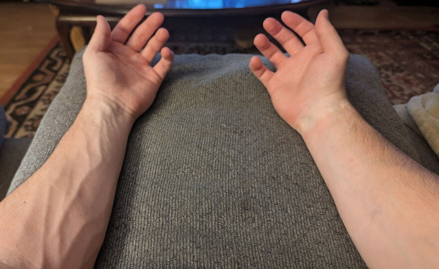 Close up of two forearms and open hands resting on a grey fabric, highlighting prominent veins, a common human body quirk.