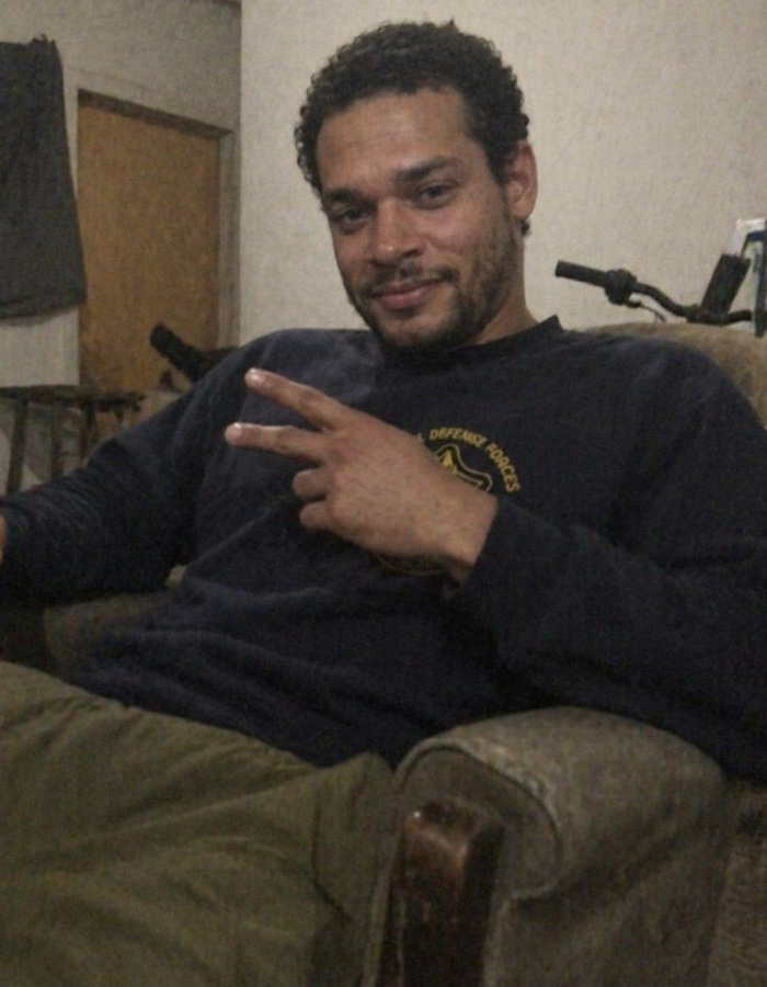 A man with curly hair and a beard, wearing a dark blue shirt, makes a peace sign. California teacher.