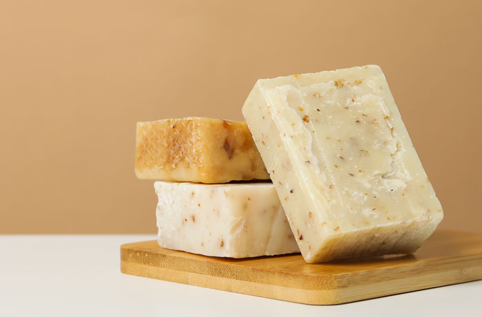 Three bars of natural, handmade soap with specks of botanicals on a wooden board. Keeping an office workspace clean.