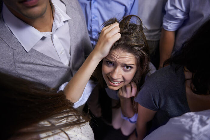 A young woman looking distressed, surrounded by people in a crowd, symbolizing disturbing sounds or an unsettling situation.