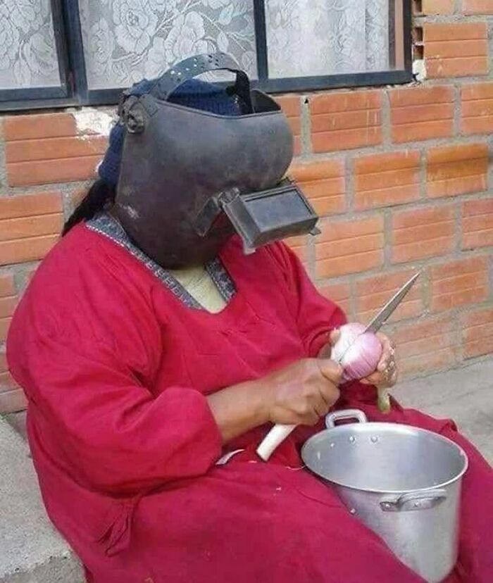 A person in a welding helmet and red dress peeling an onion, a truly weird image that lives rent-free in your mind.