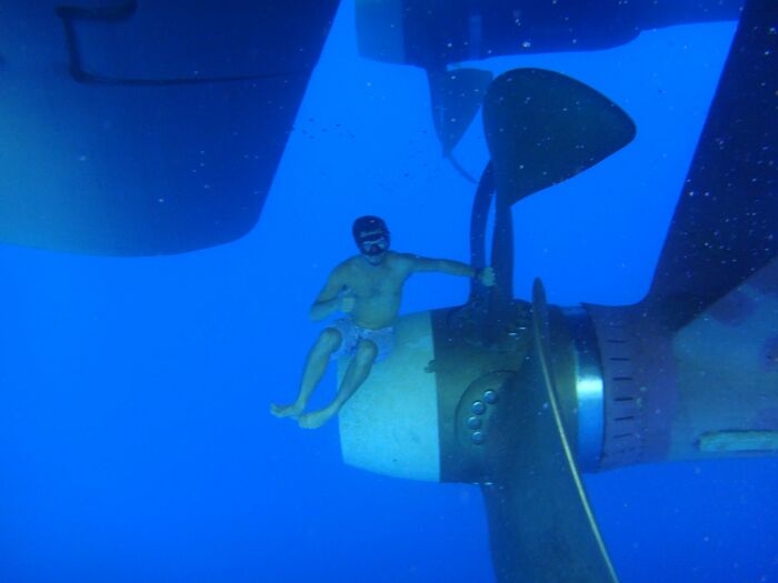 A man in a mask sits on a giant boat propeller underwater, making him feel small. Uncomfortable water pics.