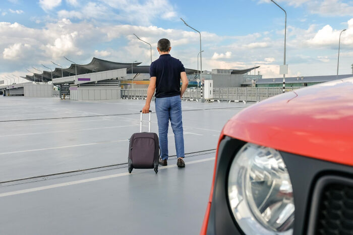 Man with suitcase on rooftop parking lot near airport, representing TSA confiscation of unusual items from travelers.