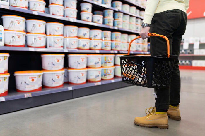 Person holding black shopping basket in a store aisle filled with stacked buckets, illustrating being a good person betrayed.