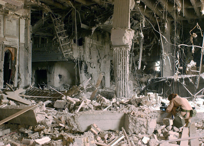 Ruins of a collapsed building with debris and a person inspecting the damage in a historical context from 1960 to 2010.