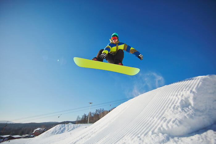 Snowboarder mid-air, a celebrity relative of nature, performing a trick against a clear blue sky, demonstrating skill and cost.