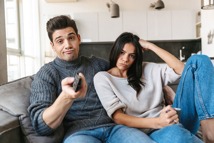 Couple sitting on couch looking upset as man holds remote, reflecting tension from dangerous traps at home situation. Couple sitting on couch looking upset as man holds remote, reflecting tension from dangerous traps at home situation.